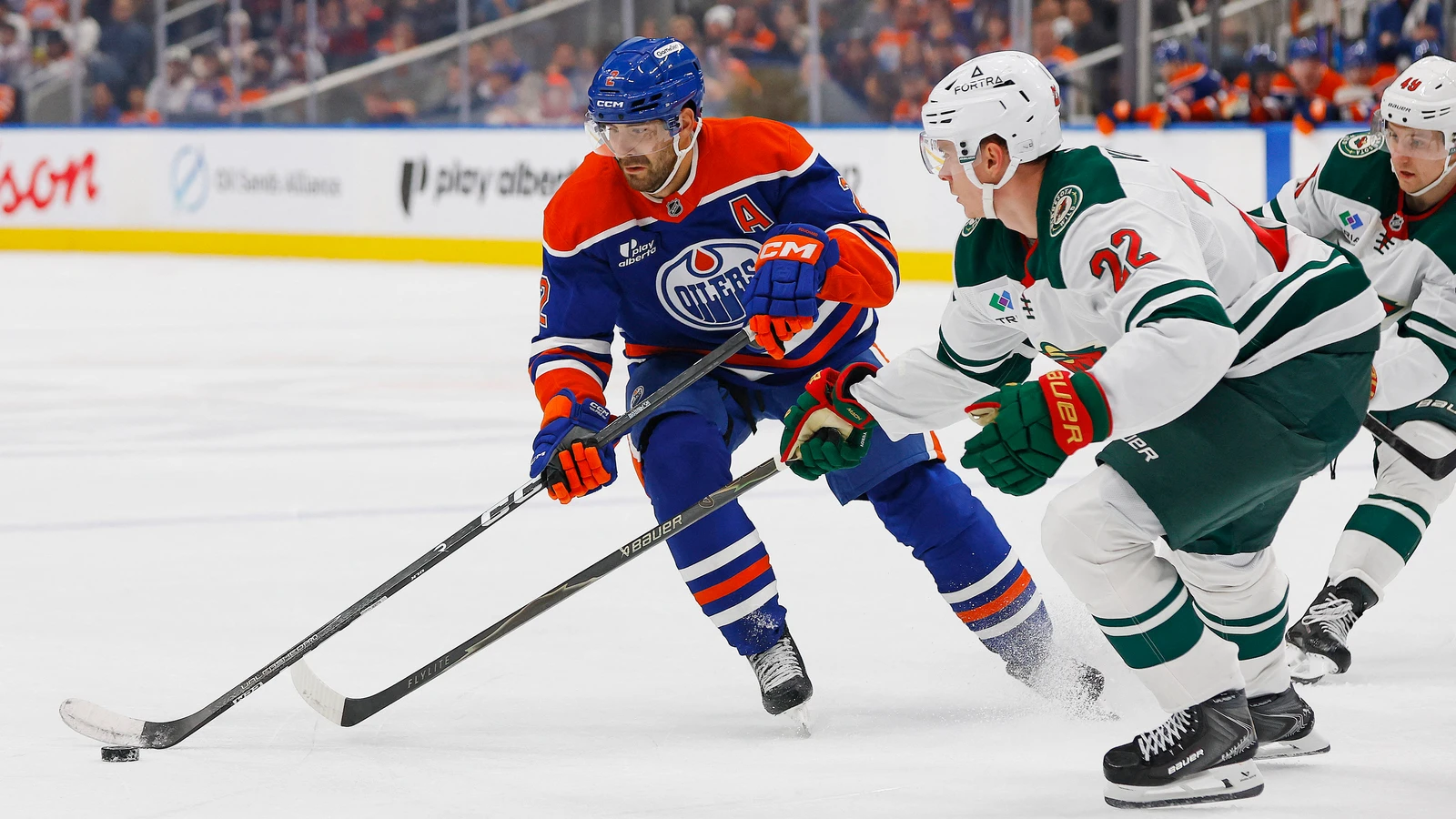 Edmonton Oilers defenceman Evan Bouchard plays the puck past Minnesota Wild forward Danila Yurov at Rogers Place.