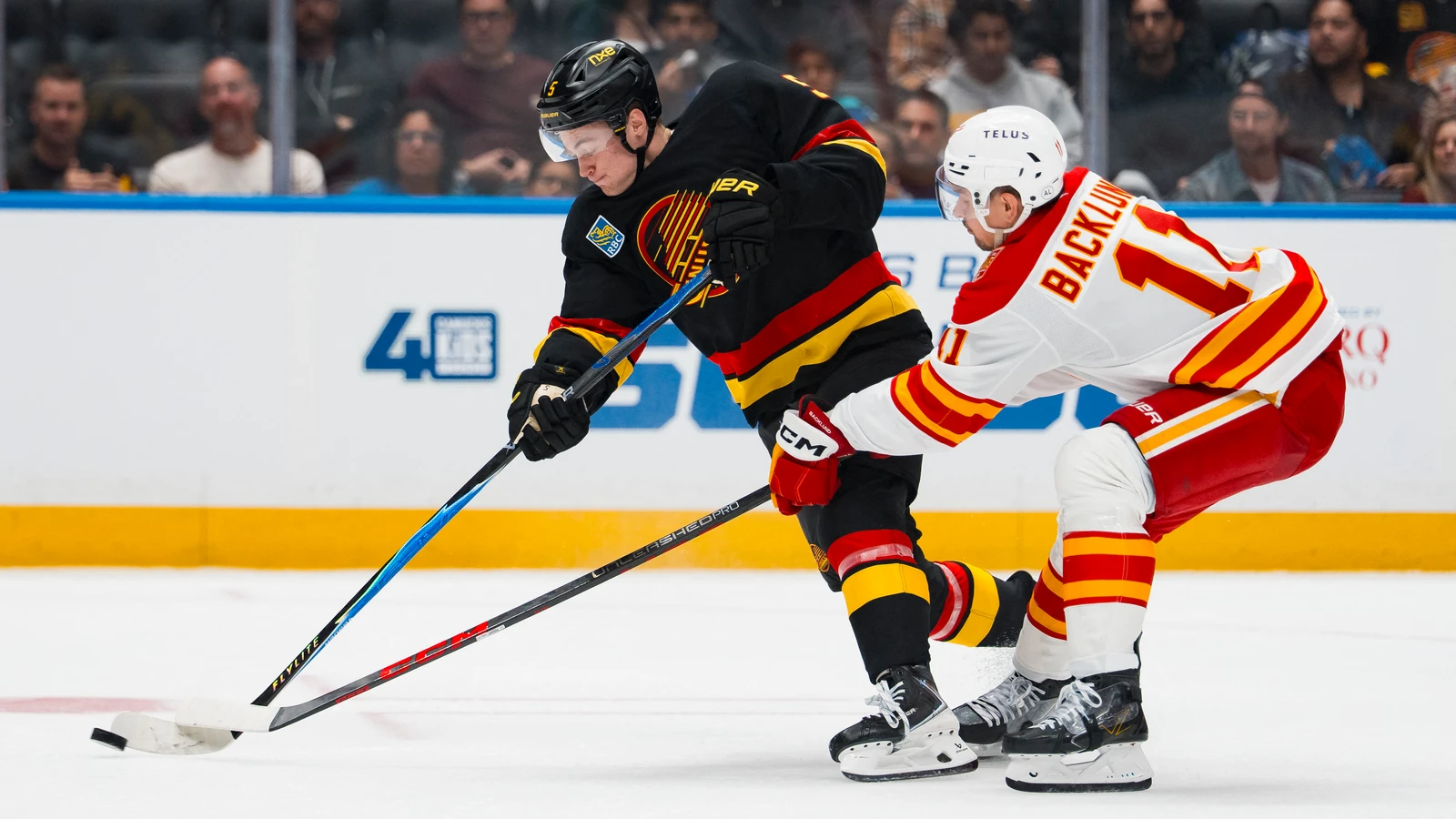 File photo: Vancouver Canucks defenceman Tom Willander handles the puck as Calgary Flames forward Mikael Backlund checks his stick at Rogers Arena.