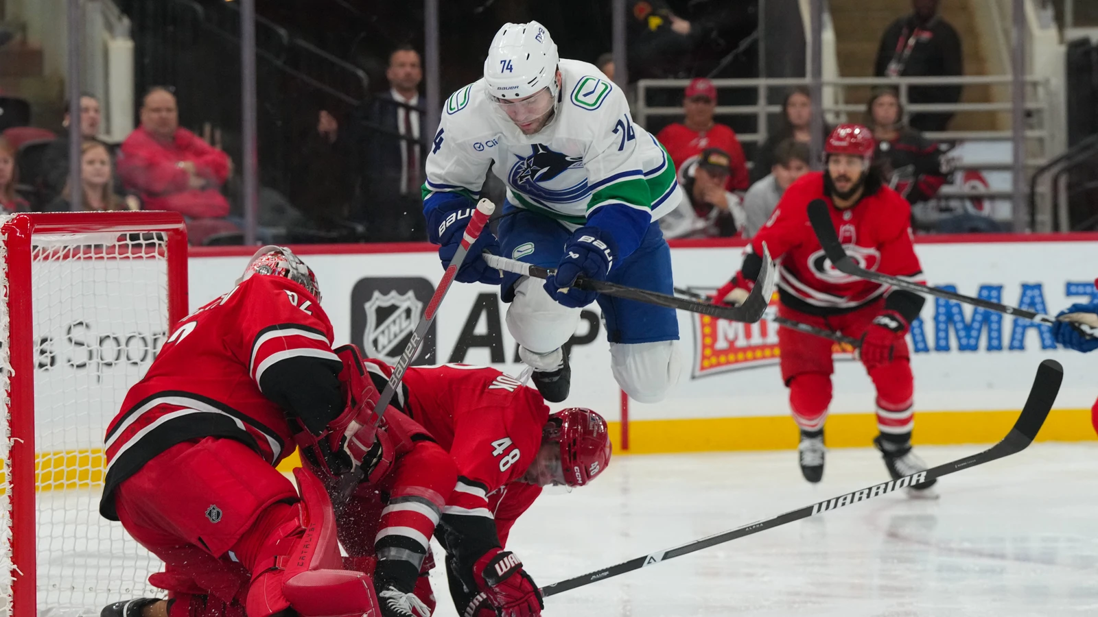 Vancouver Canucks forward Jake DeBrusk jumps over a sliding Carolina Hurricanes player at Lenovo Center.