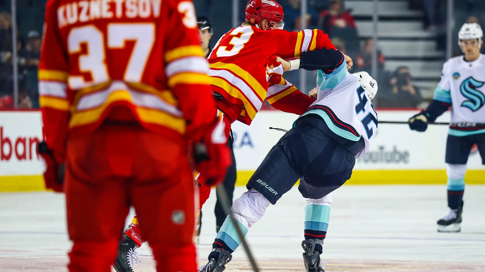 Flames forward Adam Klapka and Kraken forward Curtis Douglas trade punches during the first period at Scotiabank Saddledome as a Calgary teammate looks on.