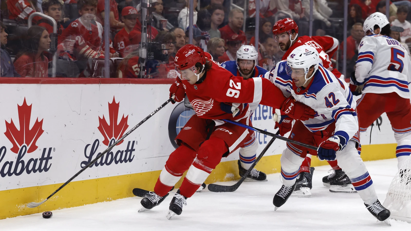 File photo: Red Wings centre Marco Kasper reaches for the puck along the boards against Rangers centre Noah Laba at Little Caesars Arena in Detroit.